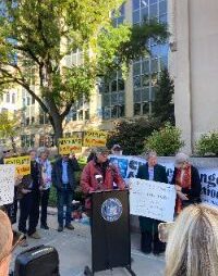 Man at podium, speaking at an outside rally, campaigning against gas pipelines.